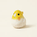 Small plush toy resembling a bird with a yellow head and white body on a beige background